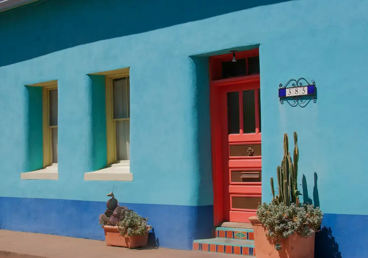 Blue stucco house with a red door and cactus out front