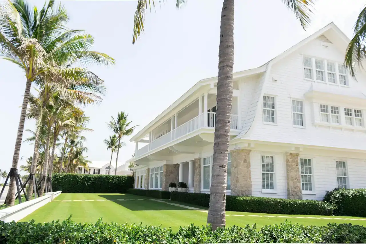 White two-story house with palm trees and a lawn