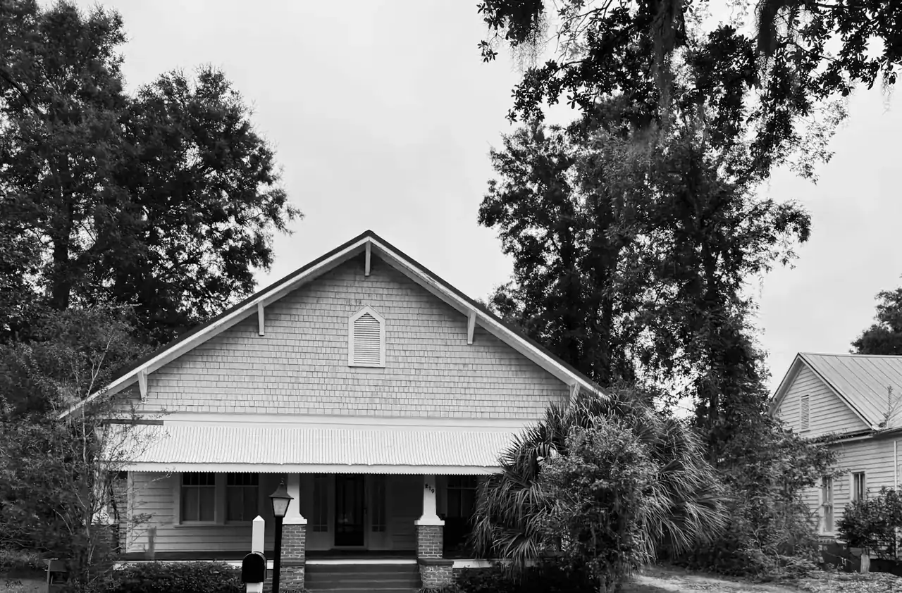 Older Southern house with a wide front porch under big trees